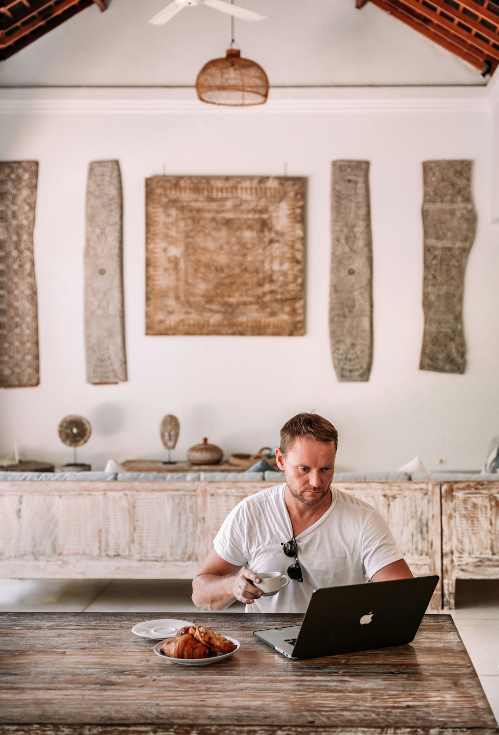 Man working on laptop at table with coffee and croissants.