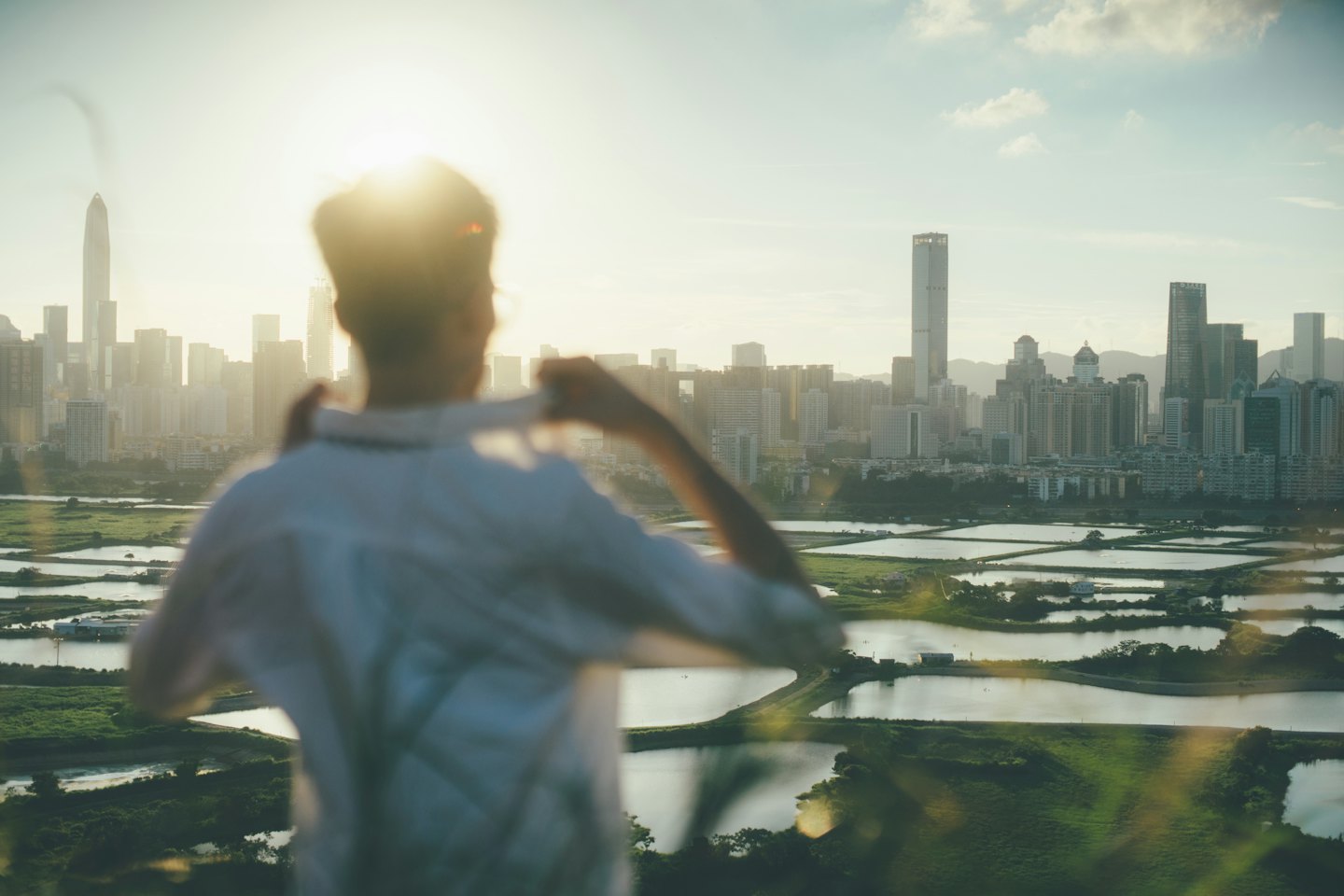 Person in a light shirt looks out over an urban cityscape.
