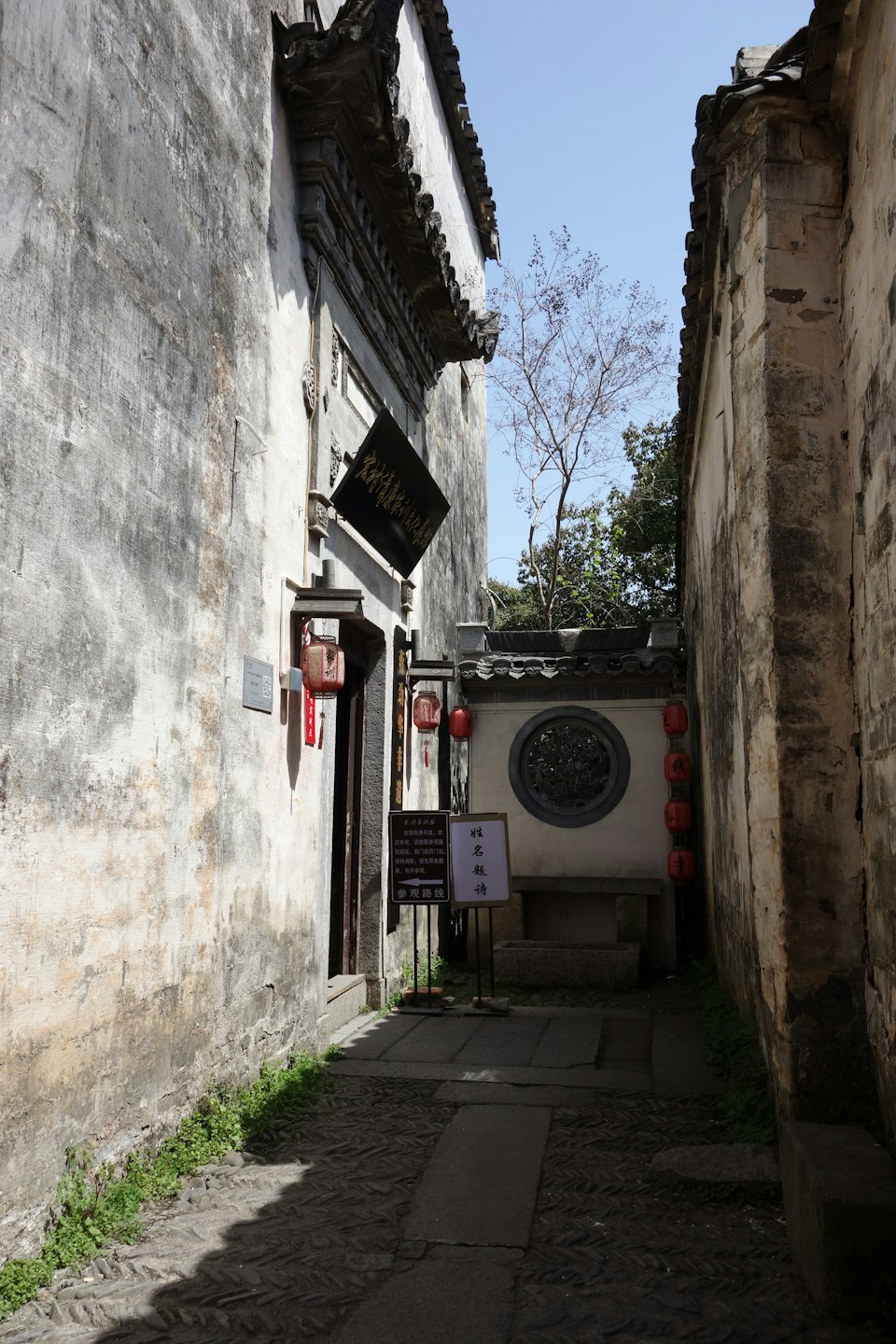 Red lanterns hang over a stone alleyway between traditional buildings.