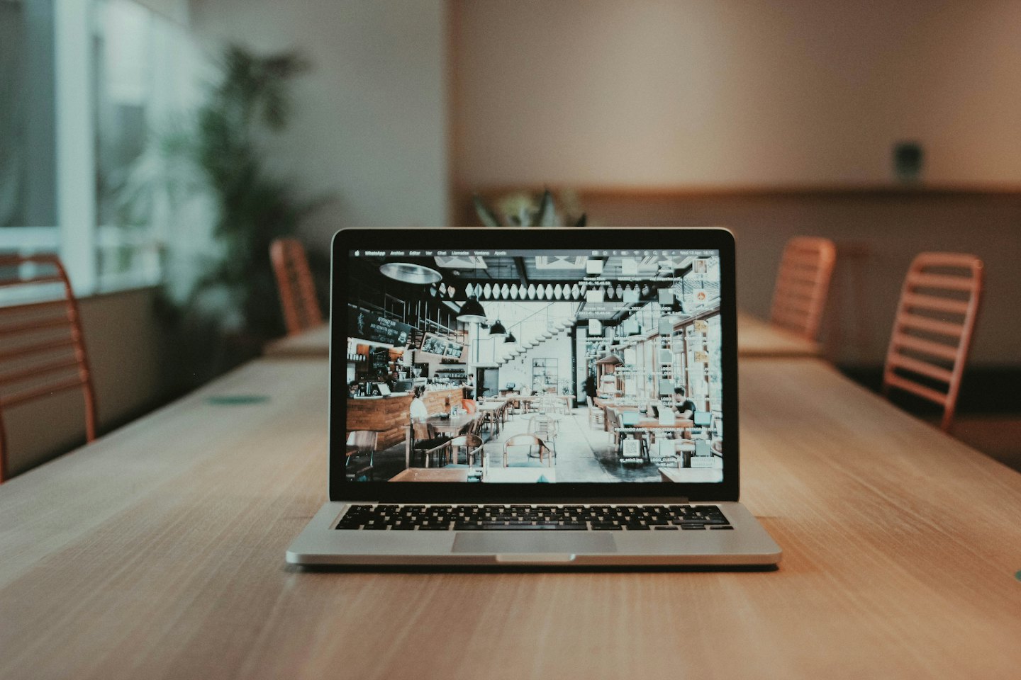 Laptop displaying cafe interior on a light wood table.