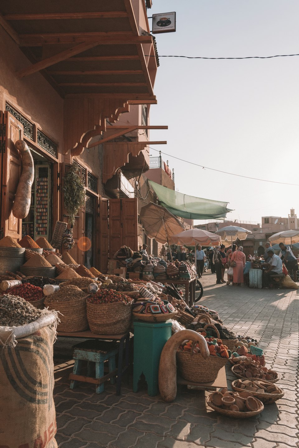 Outdoor market stalls display spices, pottery, and crafts.