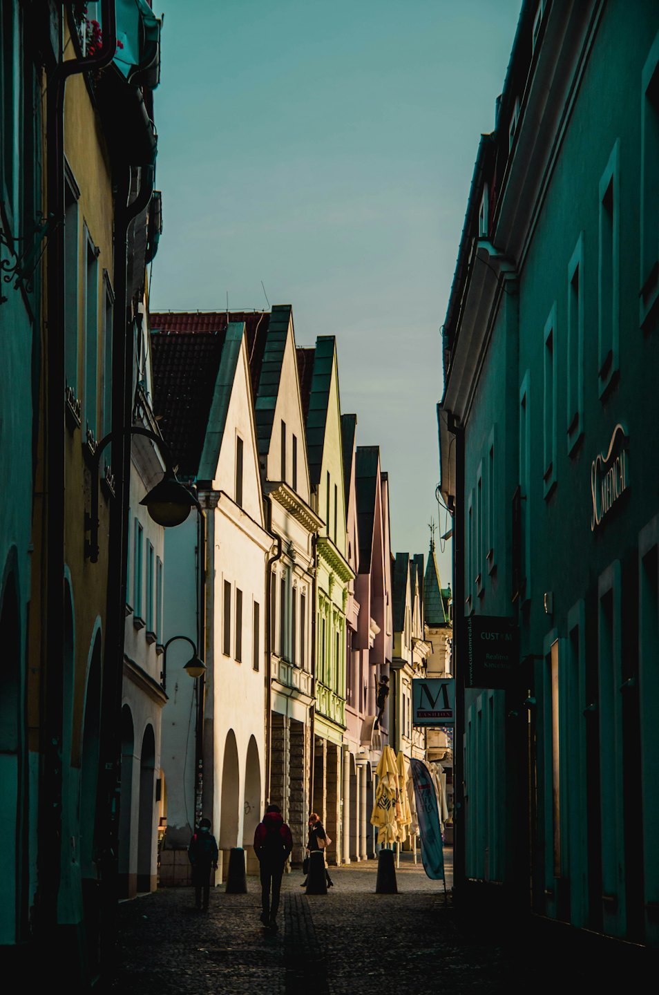Three people walk along a historic cobblestone street lined with buildings.